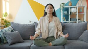 Mulher meditando de olhos fechados com fones de ouvido no sofá