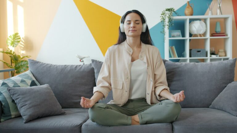 Mulher meditando de olhos fechados com fones de ouvido no sofá